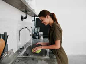 Woman smiling with teeth hands without gloves washes dishes plate with a bubble dishwashing sponge, household chores, no dishwasher, high water consumption. Stylish kitchen design, house cleaning